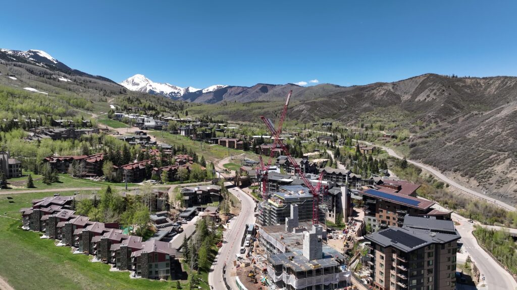Progress continues at Stratos as both buildings take shape, with facade installation and structural work advancing across the site beneath clear spring conditions. Mount Daly stands prominently in the background overlooking Snowmass Base Village.